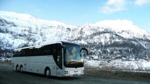 Autobus zájezdové dopravy jedoucí po silnici kolem zasněžených kopců