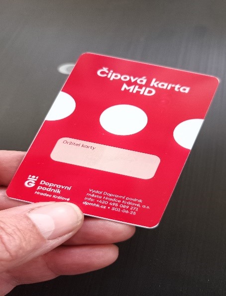 A red public transport chip card with white circles, held in the fingers of a hand, with no cardholder filled in.