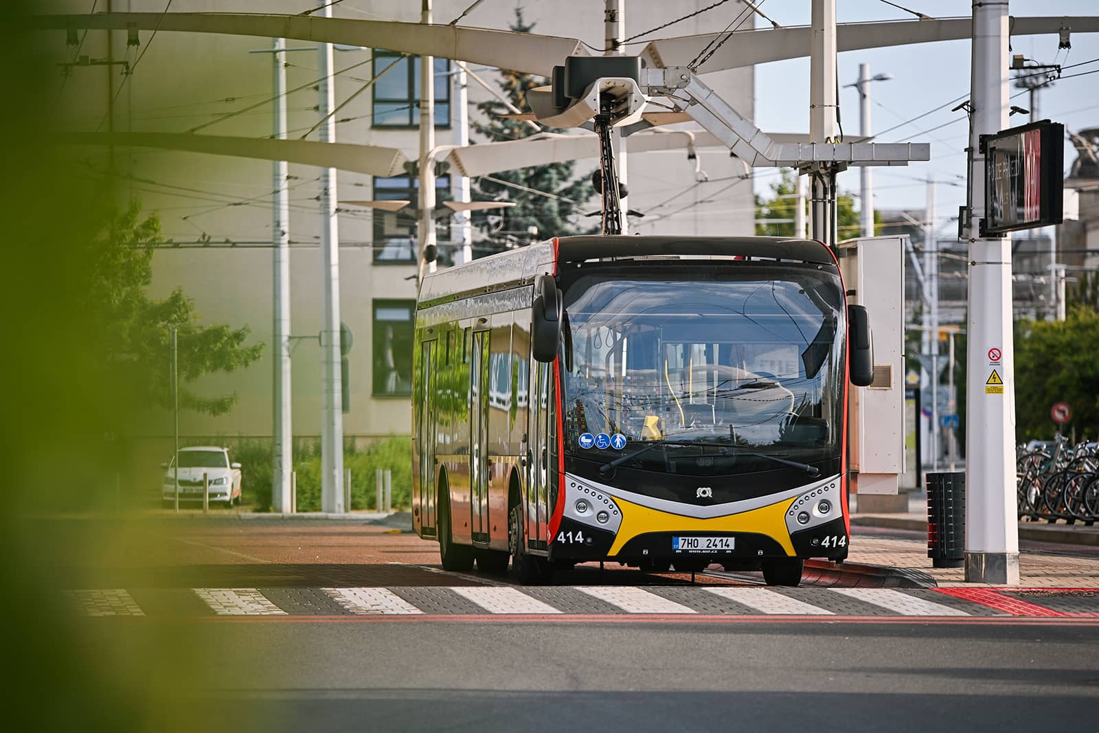 The modern low-floor electric bus with registration number 414 and registration mark 7H0 2414 is parked at the stop connected to a quick charger.