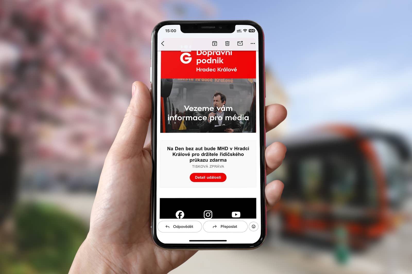 Ruka drží chytrý telefon se zobrazeným e-mailovým newsletterem Dopravního podniku. Na displeji je vidět nadpis „Vezeme vám informace pro média“ a tisková zpráva: „Na Den bez aut bude MHD v Hradci Králové pro držitele řidičského průkazu zdarma“.