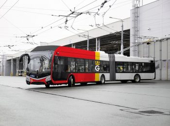 Trolejbus MHD s novým designem - polep se svislým červeným, žlutým a bílým pruhem vyjíždějící z haly